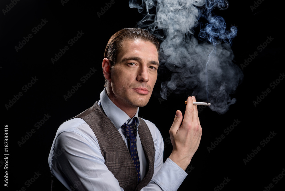 Just relax. Modish charming successful businessman is standing and holding cigarette. He is looking at camera confidently. Isolated background Just relax. Modish charming successful businessman is standing and holding cigarette. He is looking at camera confidently. Isolated background