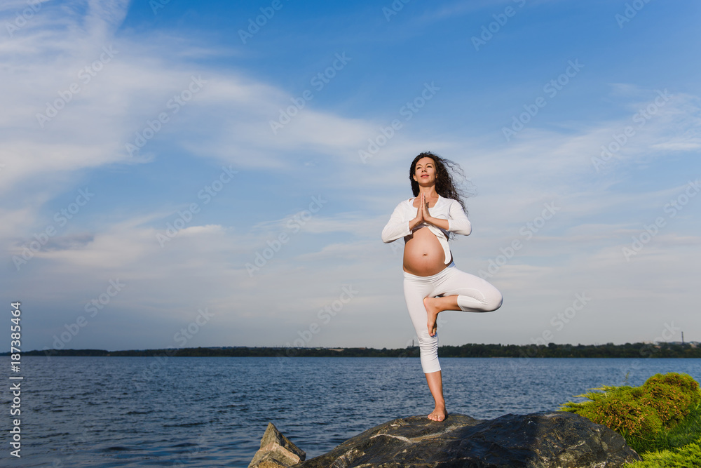 Yoga tree pose by pregnat woman.