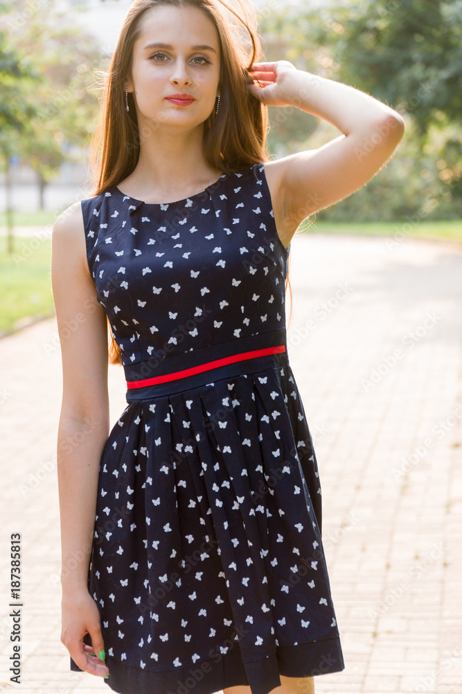 Young, beautiful, attractive woman in a stylish dress, posing on camera. She laughs, poses for the camera, her hair blowing in the wind, looking very happy
