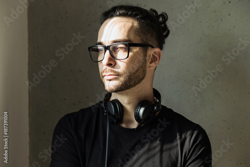Handsome man in his early 40 in a black t-shirt wearing glasses and headphones around his neck