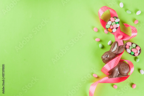 Easter holiday greeting card background, with chocolate easter bunny, candy eggs, quail eggs and festive ribbon, copy space top view