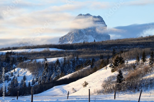 Chief mountain surrounded by a bed of low lying clouds and a fresh snow fall that covers the valley below