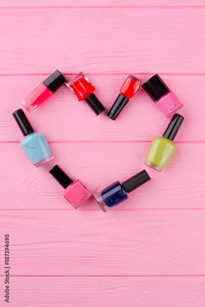 Heart made from nail polish bottles. Image of heart from decorative cosmetics accessories on pink wooden background. Nail polish composition on wooden tbackground. Love and beauty concept. Heart made from nail polish bottles. Image of heart from decorative cosmetics accessories on pink wooden background. Nail polish composition on wooden tbackground. Love and beauty concept.