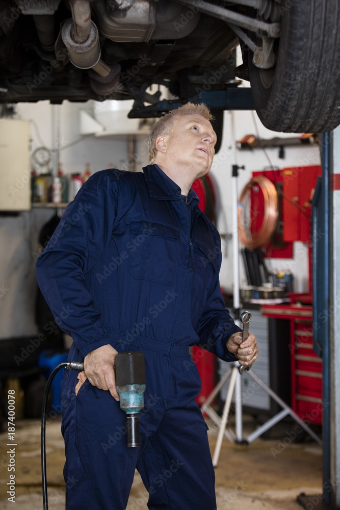 Mechanic With Hand Tools Examining Car In Garage Mechanic With Hand Tools Examining Car In Garage