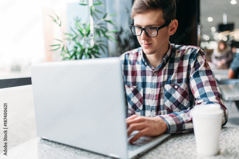 A man sits in a cafe and working on laptop, looking for work, the student writes the homework, a guy in a shirt and glasses A man sits in a cafe and working on laptop, looking for work, the student writes the homework, a guy in a shirt and glasses