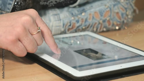 Close-up of unknown student girl dressed in denim jacket sits at desk at office the resting and looking at favorite photos using the screen of computer tablet in white-black colour. photo