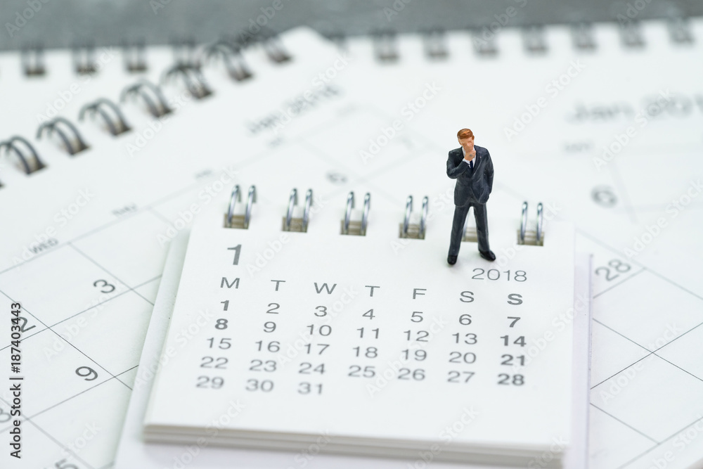 Miniature businessman thinking and standing on calendars using as business goals or future thinking Miniature businessman thinking and standing on calendars using as business goals or future thinking