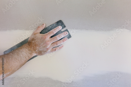 Man's hand sanding plasterboard in home renovation