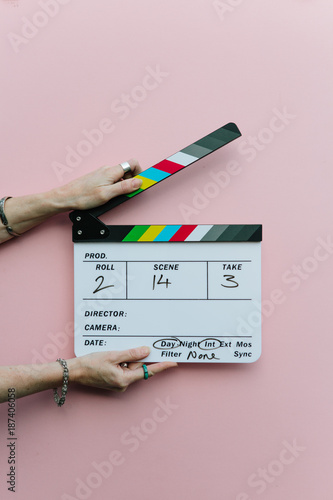 Woman holding clapperboard over pink background photo