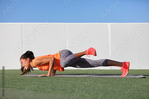 Yoga fitness girl training triceps doing advanced push-up chaturanga with leg side crunch spiderman pose. Pushup exercise variation workout Asian woman on exercise mat outdoors. Happy active person.