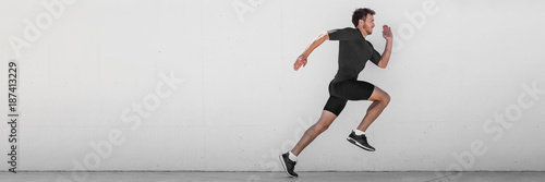 Running man runner training doing outdoor city run sprinting along wall background. Urban healthy active lifestyle. Male athlete doing sprint hiit high intensity interval training. Banner panorama. photo