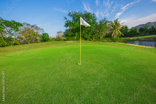 White flag, golf ball and green grass under blue sky at the beautiful course as goal concept