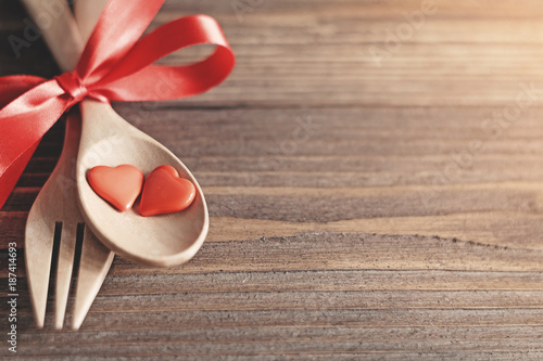 Wooden spoons and forks are strapped together with a bright red ribbon,red heart in wooden spoon placed on a wooden background,dinner for lover in valentines day.