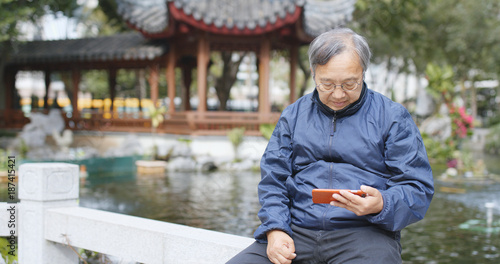 Photography Asian old man use of mobile phone and sitting at chinese garden