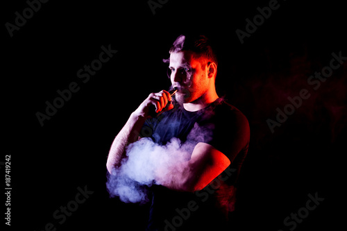 Fototapeta Naklejka Na Ścianę i Meble -  vaping man holding a mod. A cloud of vapor. Black background.
