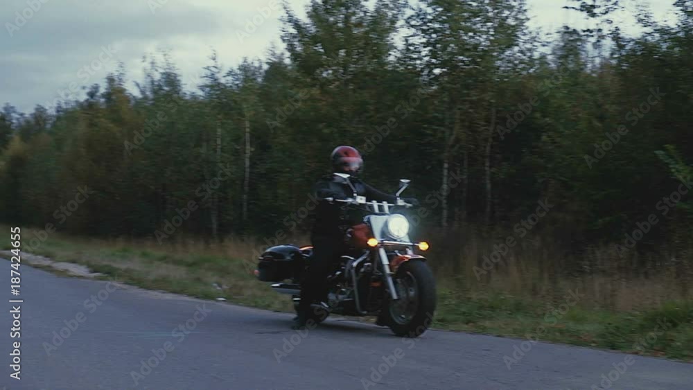 A man rides a motorcycle down a road in forest A man rides a motorcycle down a road in forest