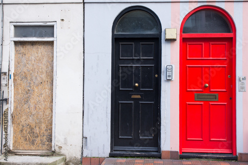 Black door next to a red door and a wooden panel replacing a missing door in the front facade of a Victorian British English house