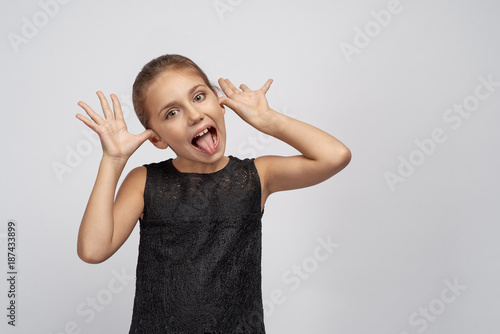 Little naughty kid with black hair shows tongue in protest, the girl misbehaves, her tongue in sign of mockery and shows the owner that you are a fool