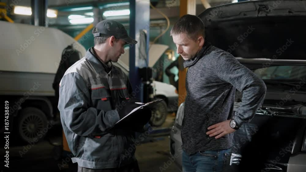 The adult man turned to the machine service for repairing his minivan, the driver is talking to the repairman The adult man turned to the machine service for repairing his minivan, the driver is talking to the repairman