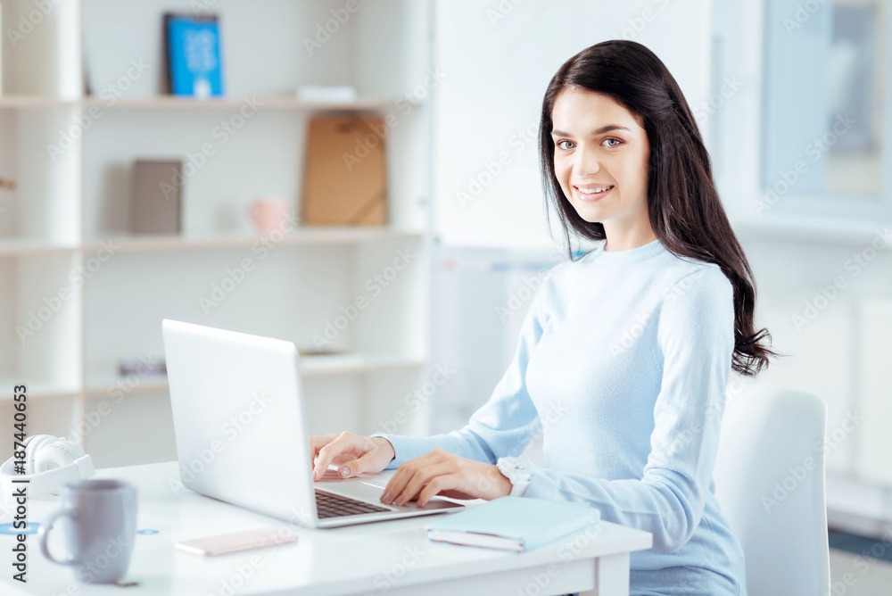 Pleasure in study. Happy young female student sitting on the chair while smiling and using laptop Pleasure in study. Happy young female student sitting on the chair while smiling and using laptop