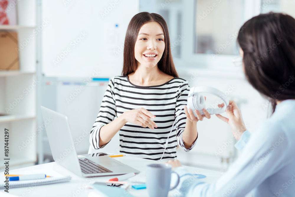 Working music. Amazed vigorous pleasant woman stretching headphones while sitting and talking to a friend Working music. Amazed vigorous pleasant woman stretching headphones while sitting and talking to a friend
