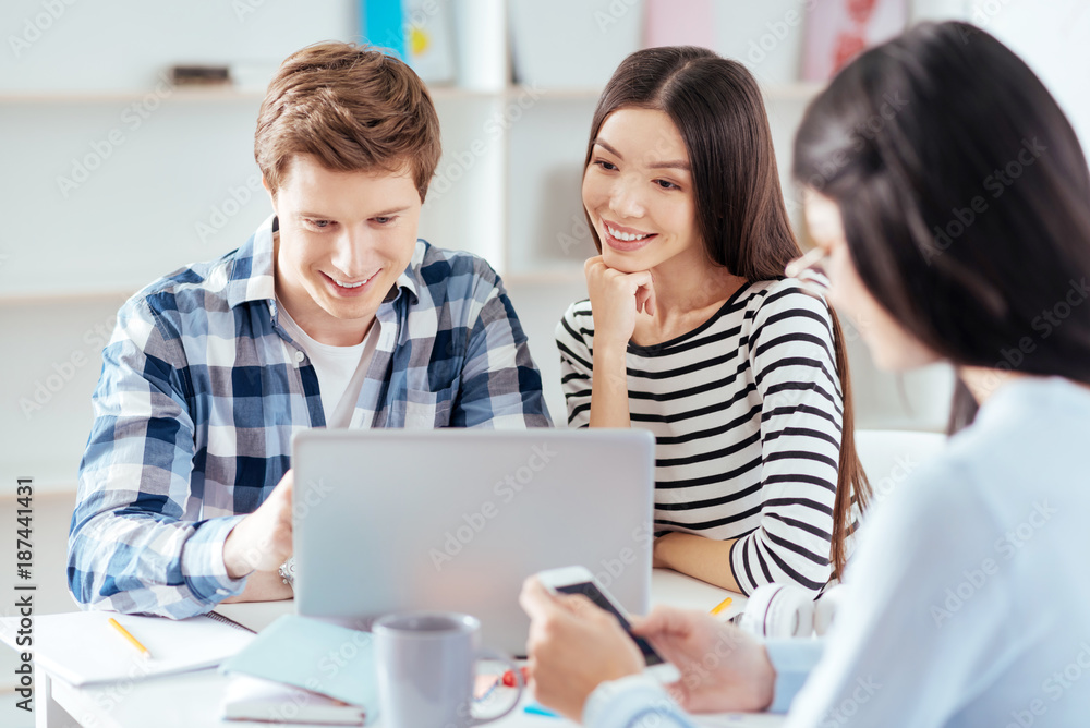 Together better. Joyful gay three students spending time together while looking at the screens and sitting Together better. Joyful gay three students spending time together while looking at the screens and sitting