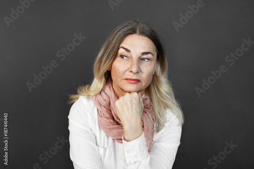 Human facial expressions, emotions, feelings, reactio, attitude and life perception concept. Serious attractive 60 year old blonde female looking away and resting chin on fist, having pensive look photo