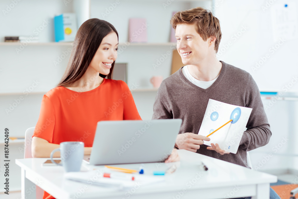 Everything right. Happy energetic two students studying economy while laughing and guy pointing at graphic Everything right. Happy energetic two students studying economy while laughing and guy pointing at graphic