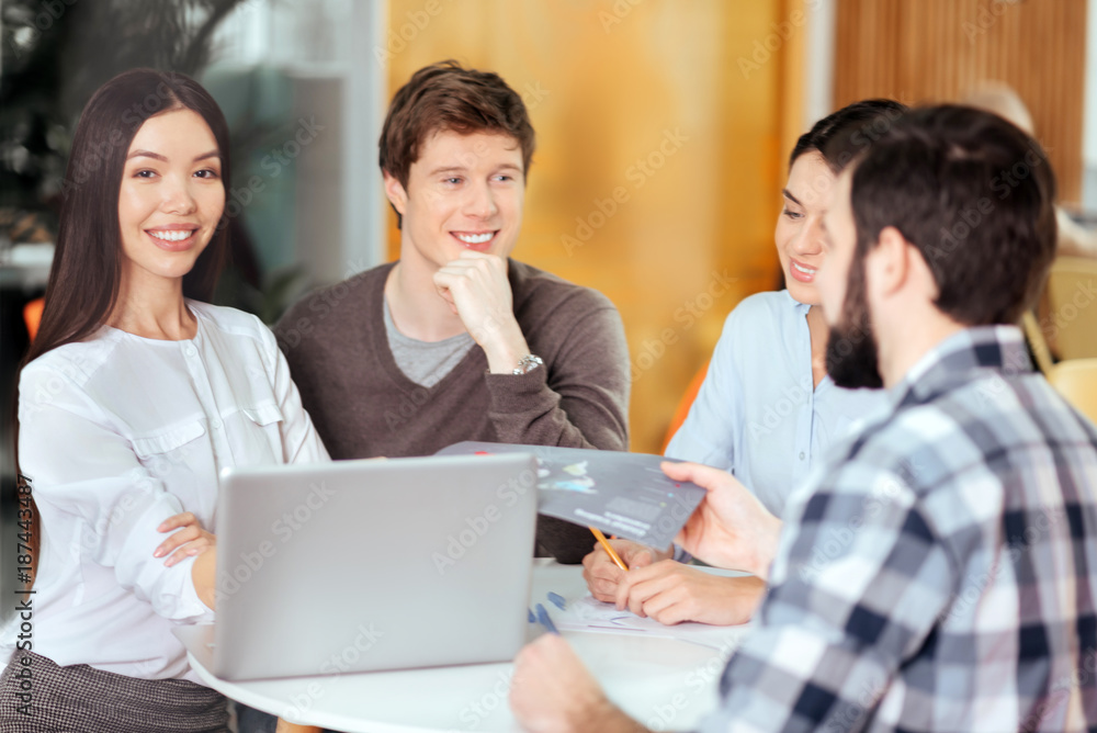 Team meeting. Joyful merry four colleagues resting at the table and conducting meeting while grinning Team meeting. Joyful merry four colleagues resting at the table and conducting meeting while grinning