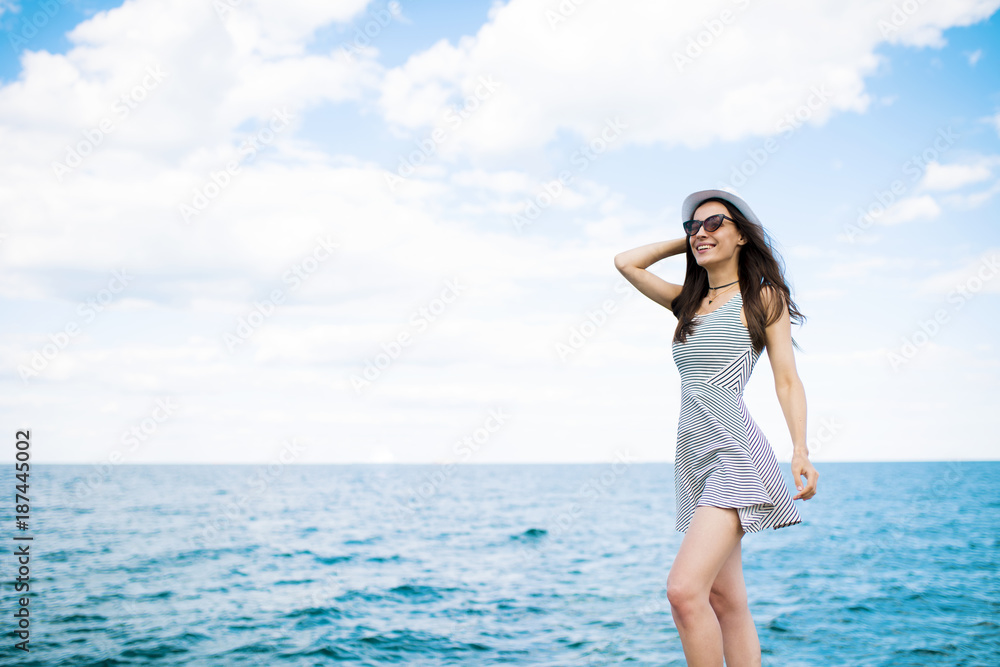 Trendy modern beautiful girl in a dress and hat posing on the beach