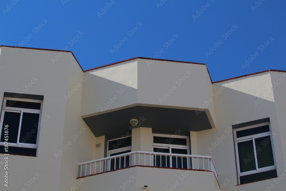 Balcony at white apartment building against blue sky