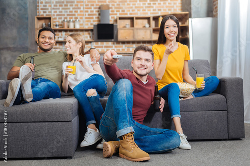 Watching TV. Positive cheerful young relaxing couples having a good time together while sitting in a comfortable room and watching TV