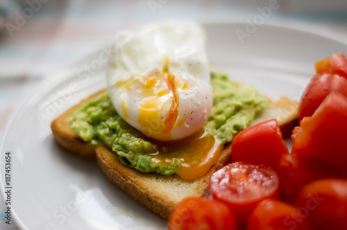 Perfect poached egg with avocado toast and fresh tomatoes on a white plate on a dish cloth