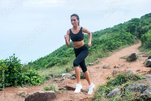 Fitness female athlete running on forest path in mountainous area in summer. Sporty woman working out going uphill.