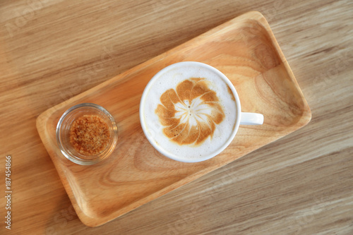 Cup of latte coffee with latte art and brown sugar on wooden tray.