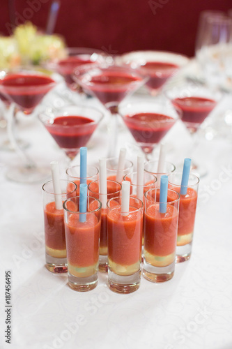 treatment  alcohol  celebration concept. close up of few small glasses for hard drinks that full of red drink  in each glass there is blue or white short straw
