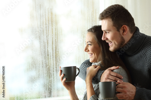 Fotografia Happy couple looking through a window a rainy day