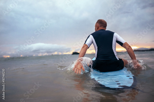Surfer sits on surfboard on the waves in sunset time