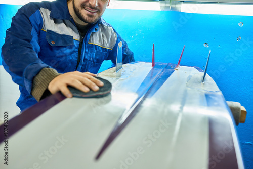 Mid-section of unrecognizable worker carefully polishing surfing board with felt disk in yacht workshop, copy space