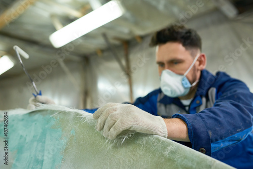 Portrait of mature man wearing protective mask repairing boat while working in yacht workshop, focus on foreground