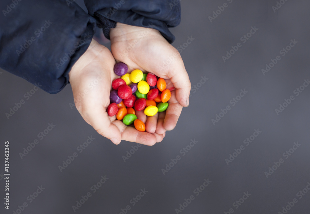 Kid's hands full of sweet multicolored candy . Dark background & copy space.