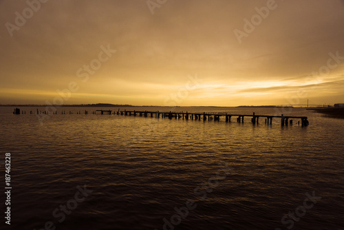 Germany, Baltic Sea, Stralsund: Atmospheric colorful sunset with sea, sunbeams, weirs, reed, horizon, sky and Strelasund Crossing Bridge in the background
