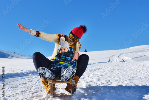 photo of happy mother and child playing in the snow with a sledge in a sunny winter day