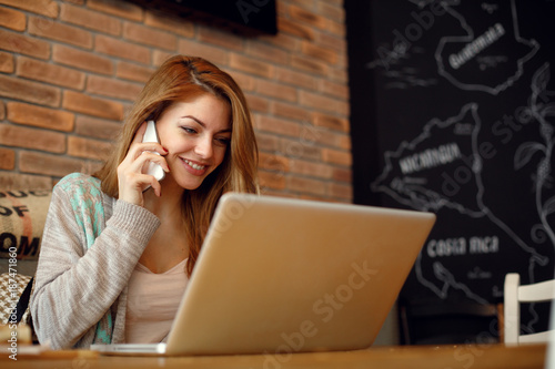 Young woman talking on the phone with a laptop on table in cafe