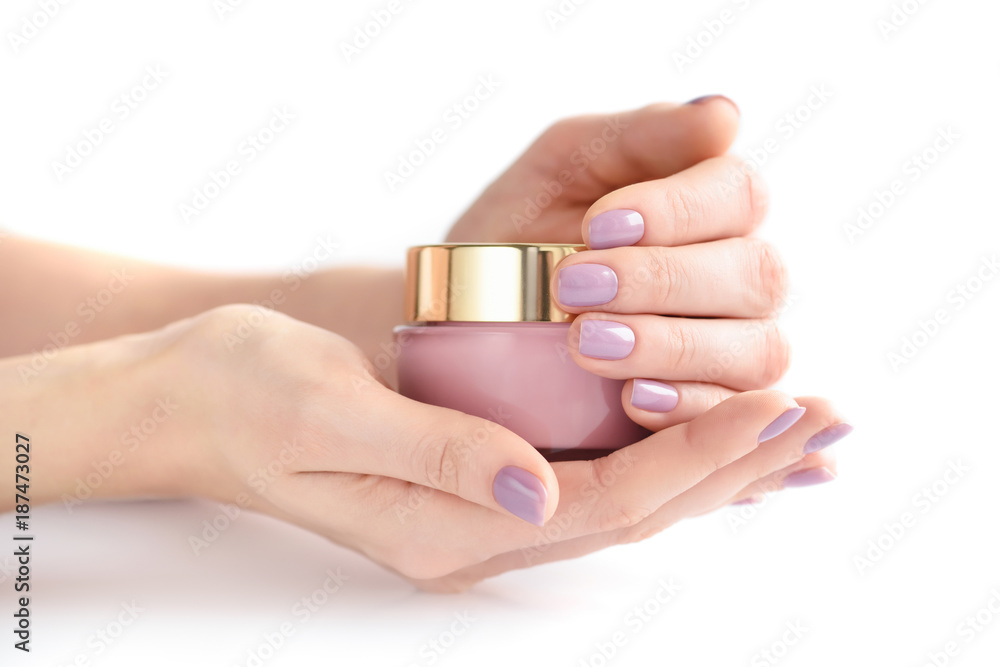 Hands of a woman with pink manicure with jar of cream on white background