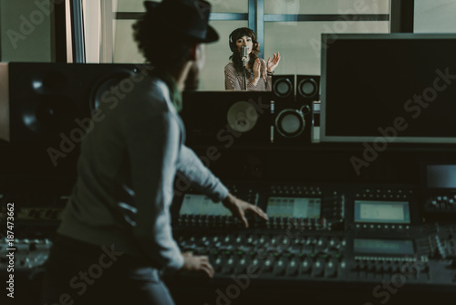 Fototapeta sound producer in hat recording song at dark studio