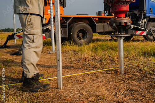 technician installing ground screw for mounting structure of solar panel at solar farm