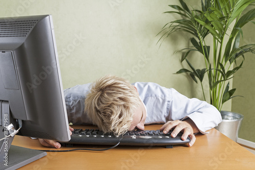 Tired man fallen asleep slumped over computer keyboard when working in office