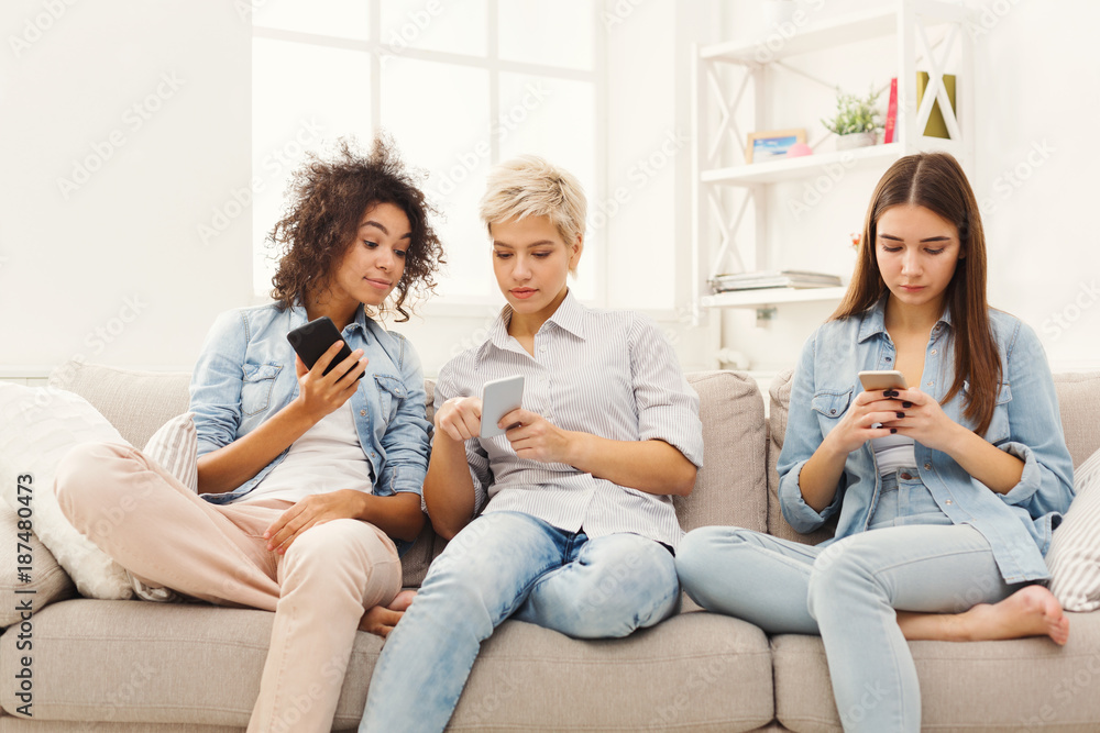 Three female friends using smartphones at home Three female friends using smartphones at home
