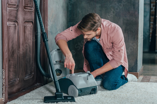 Bilde på lerret young man looking at broken vacuum cleaner and fixing it at home